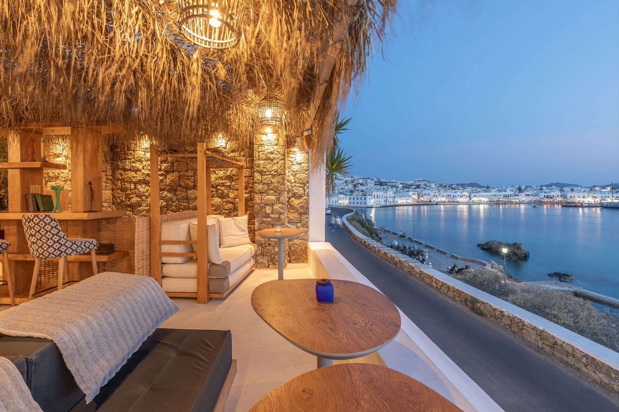 The Blu Blu veranda under its thatched roof, looking across the Old Port to Mykonos Town at dusk